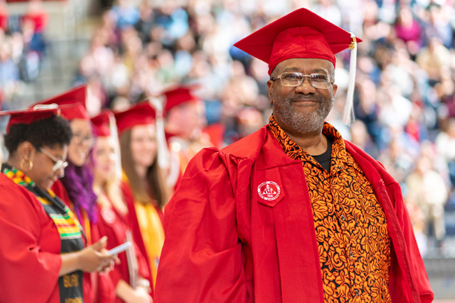 Happy SVSU graduate at a graduation ceremony wearing a red graduation gown and cap