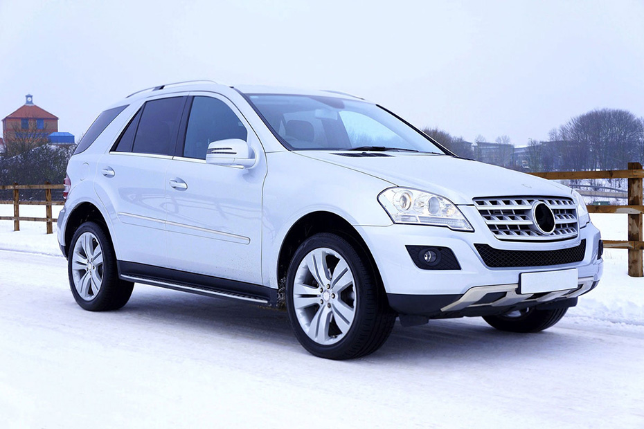 White crossover car driving down a snow covered small town road lined with a wooden fence during winter