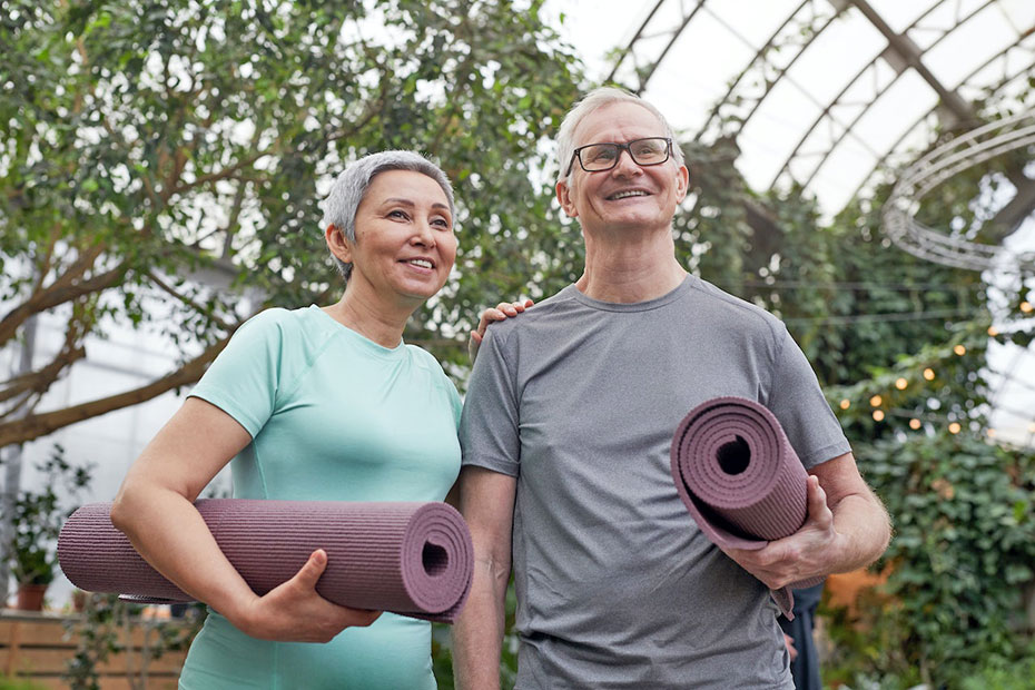 Confident senior couple holding yoga mats in a greenhouse