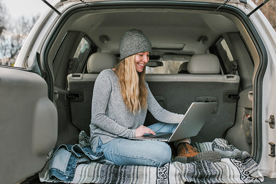 Female in her car happily using a laptop