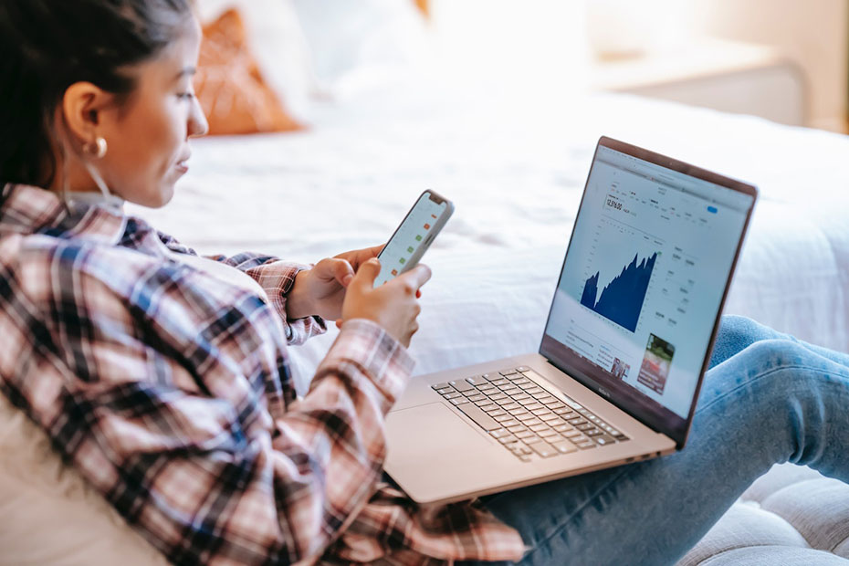 Female managing investments on her couch on computer and smartphone