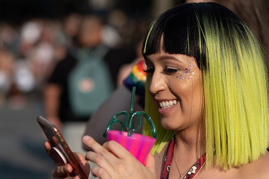 Female with her hair dyed black and light green happily looking at her phone while holding a cup