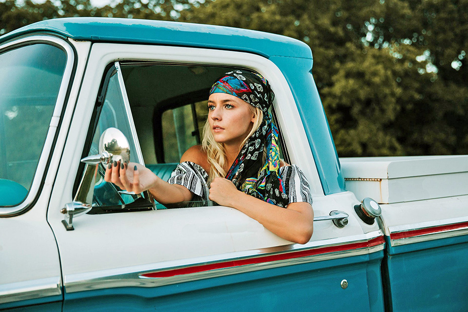 Female leaning out of her classic pick up truck's rolled down window to adjust the side mirror