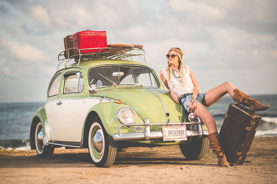 Woman with a suitcase at a beach leaning on her old fashion car