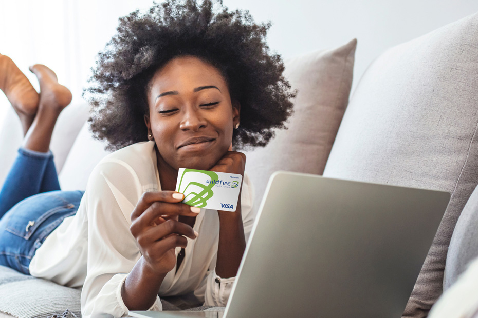 Happy woman lying on a couch on her computer holding a Wildfire credit card