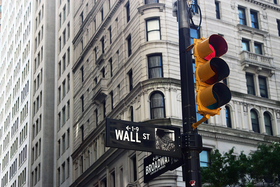 Broadway and wall Street street sign on a traffic light pole with a large building in the background