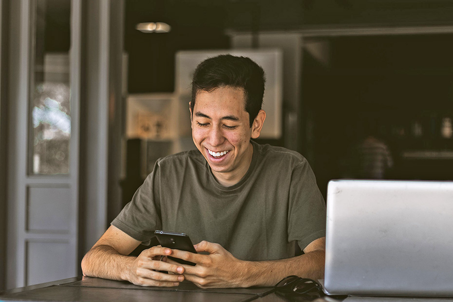 Male smiling while using a smartphone and a laptop