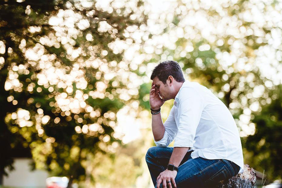 side view of a Stressed male sitting outside with his hand on his face