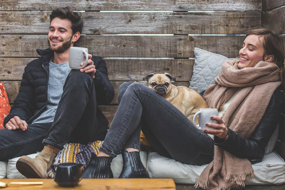 Man and woman happily enjoying their rustic style home with their dog as they sit on the couch