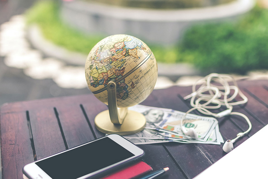 Mini globe outside on table with money and a smart phone