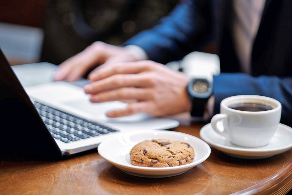 Person using laptop with a cookie sitting next to it