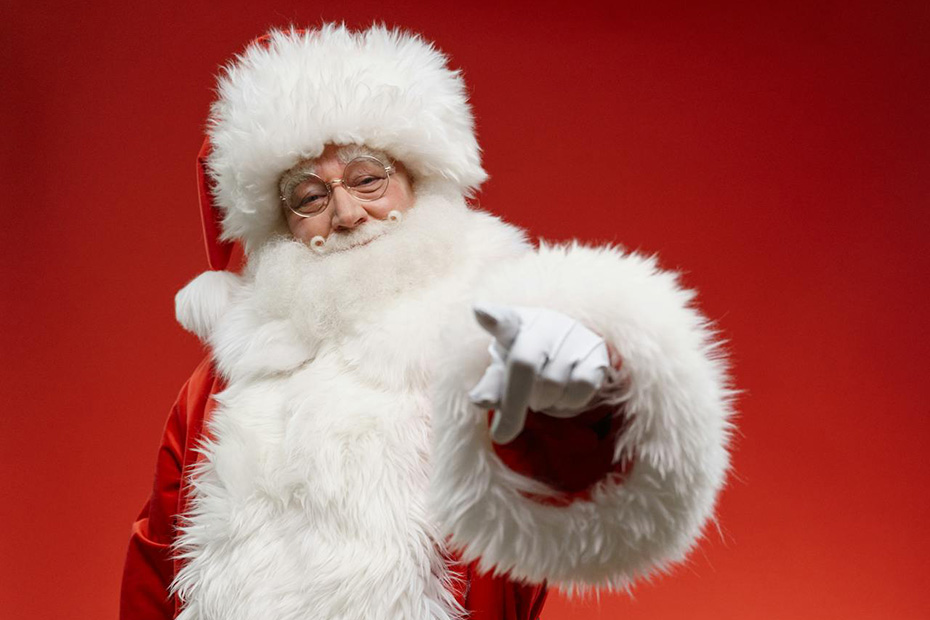 Santa Claus in front of a red back drop pointing at you