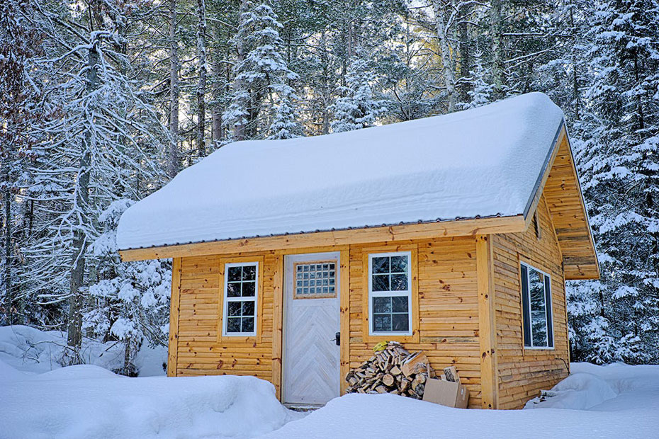 Small wood cabin home in the winter just out side a snowy forest with the roof covered in snow