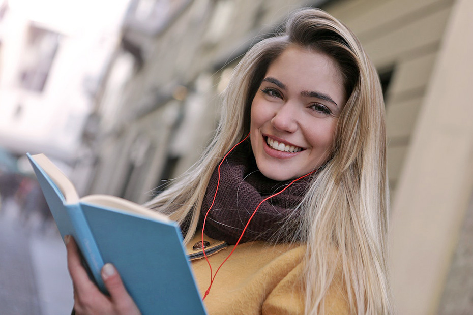 Smiling female college student wearing a coat and scarf holding a book