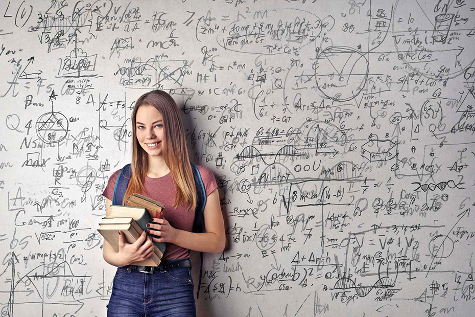 Smiling Female student holding books next to whiteboard filled with equations