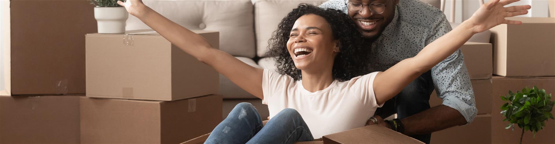 Husband pushing wife around in a box as they move in to a new home