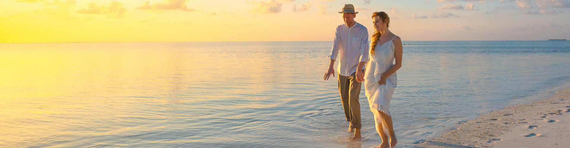 Couple walking a beach during sunset with a lighthouse in the background