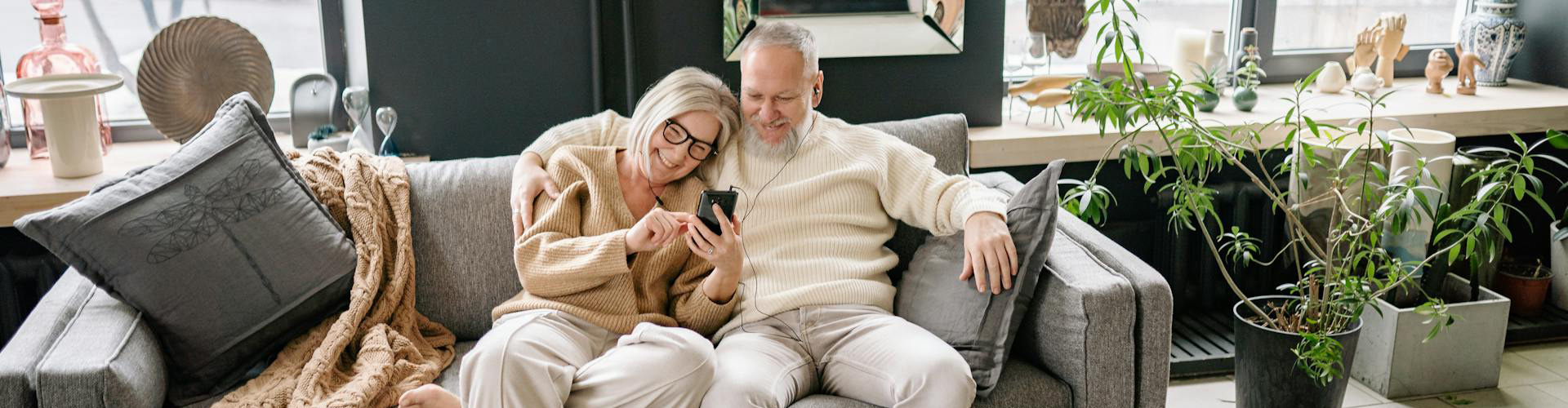 Happy senior couple sitting next to each on couch looking at smartphone