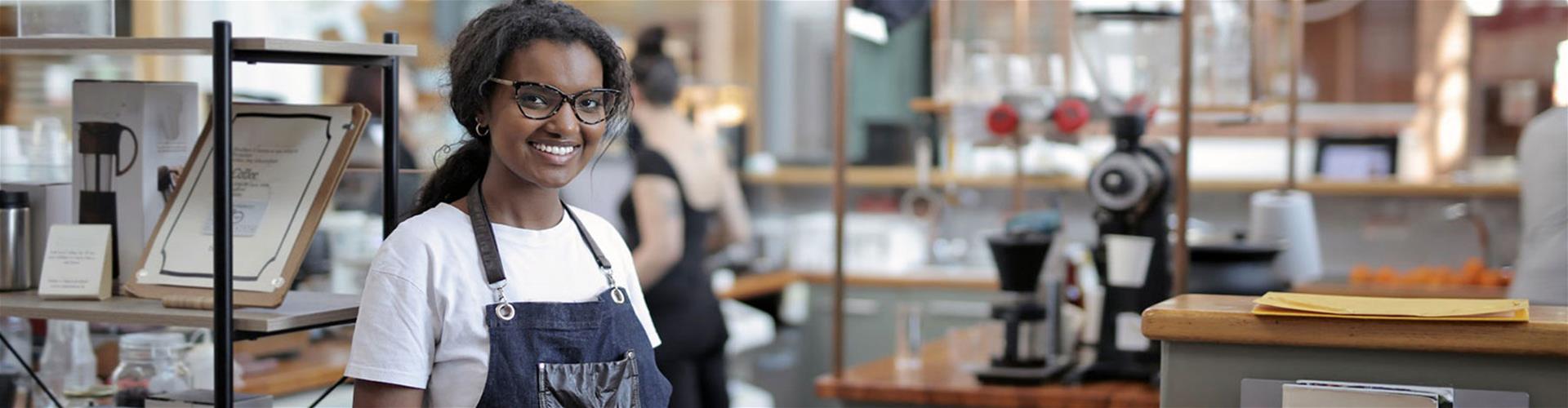 Happy woman wearing an apron standing by shelves in café