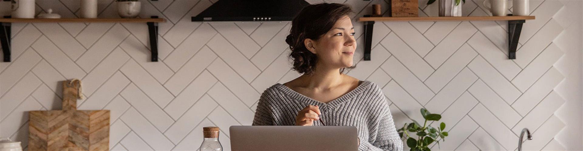 Positive young woman with laptop in cozy kitchen interior