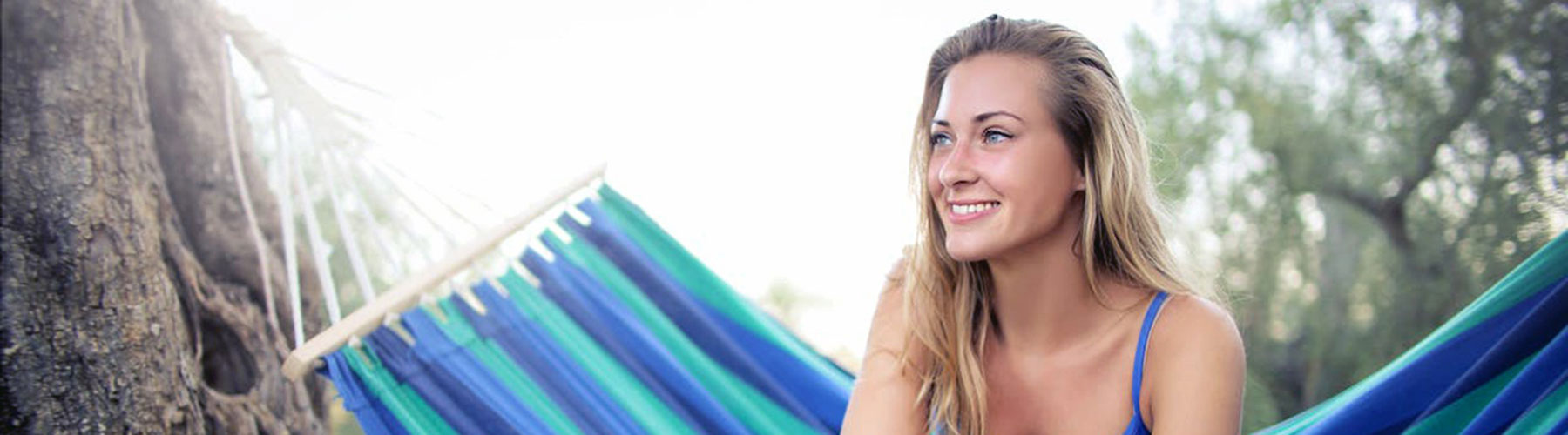 Sun shining on female smiling optimistically while sitting in a hammock in nature