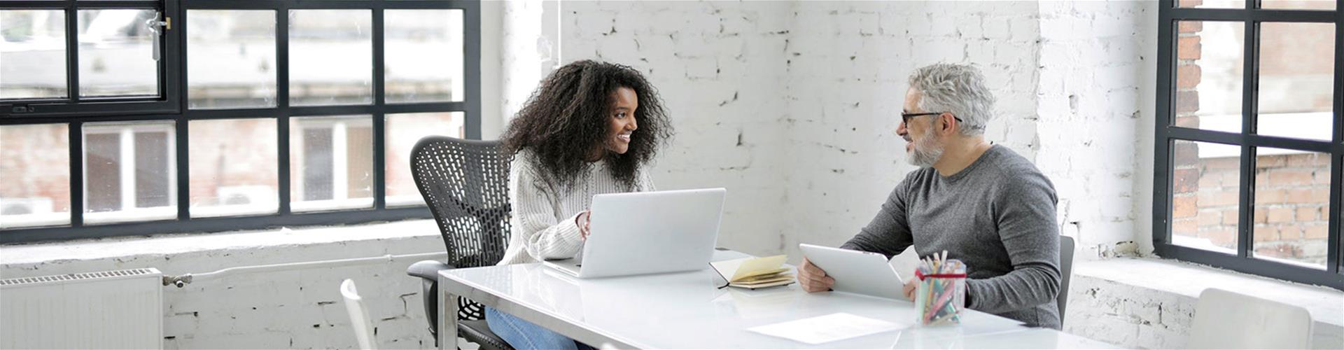 two co-workers happily working together on a laptop and a tablet