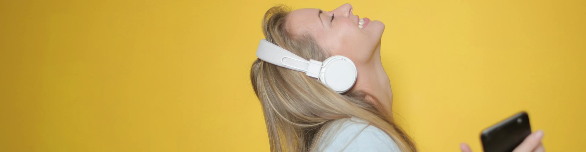 Woman happily listening to music infront of yellow backdrop