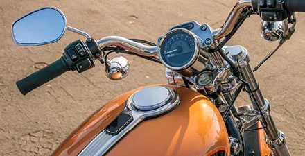 Close-up of a motorcycle handlebar and fuel tank on a dirt road.