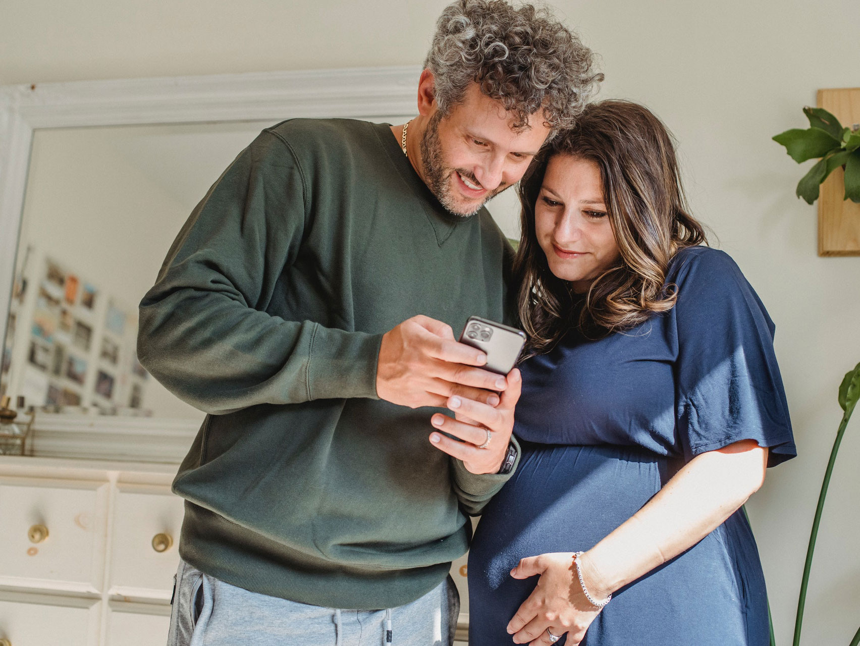 Adult man with pregnant wife watching smartphone at home