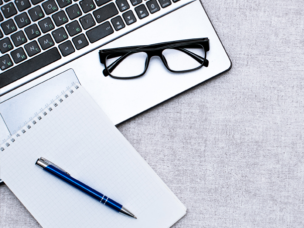 Laptop with glasses, notepad and pen sitting on top