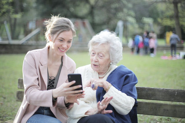 Cheerful senior mother and adult daughter using smartphone together