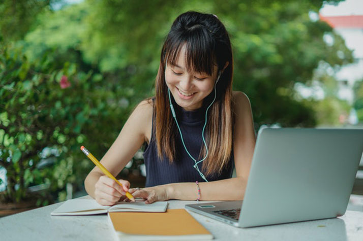 Happy female Asian student doing homework and listening to music with earphones Happy female Asian student doing homework and listening to music with earphones