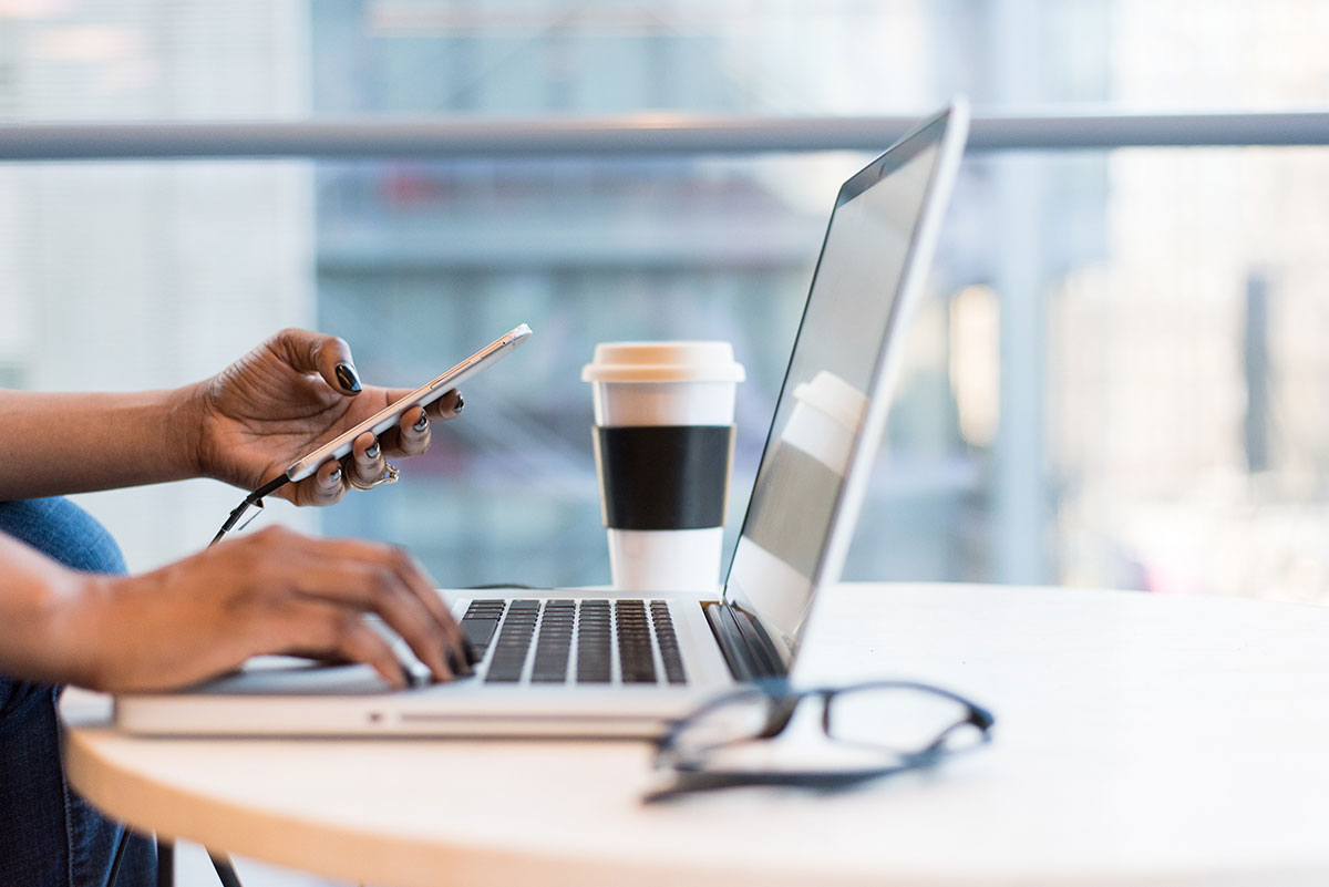 Person using a phone and computer at a table