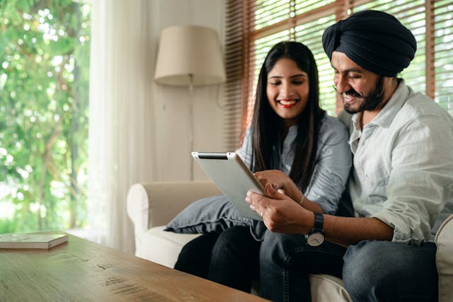 Happy couple sitting on a couch in a well lit living room using an iPad together