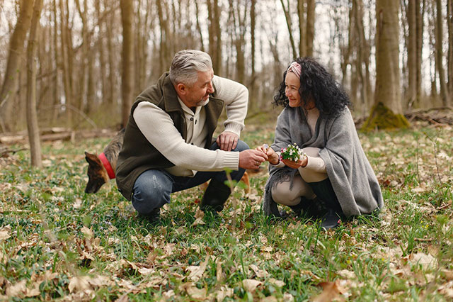 Happy elderly couple in love with fresh flowers and dog in forest