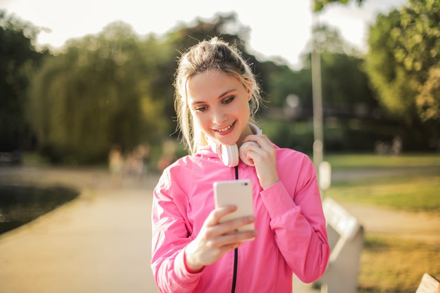 Smiling Woman in a Pink Jacket Using a White Phone and headphones