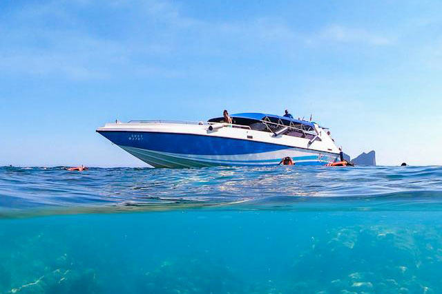 Picture half above water half below water of a speedboat in a lake with people swimming around it