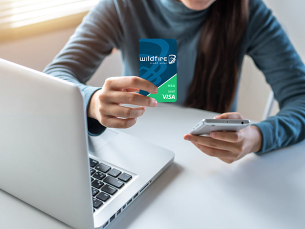 Woman on laptop and smartphone holding a Wildfire HSA Card