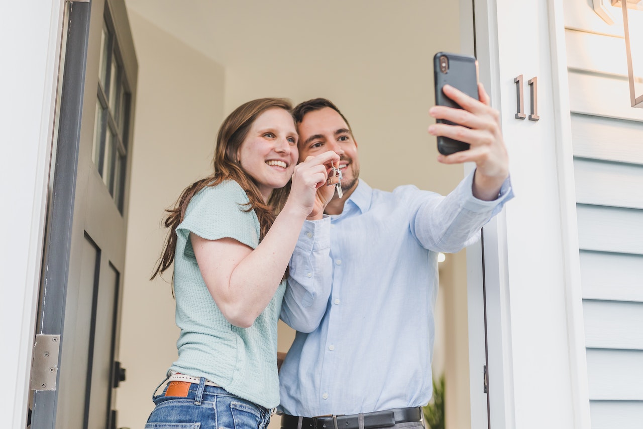 Young couple taking picture with new keys outside new home