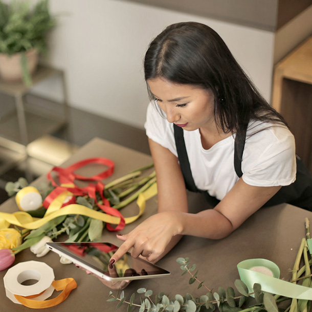 female florist on a tablet leaning on a table with flowers