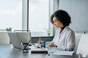 Woman sitting in office with laptop doing paperwork