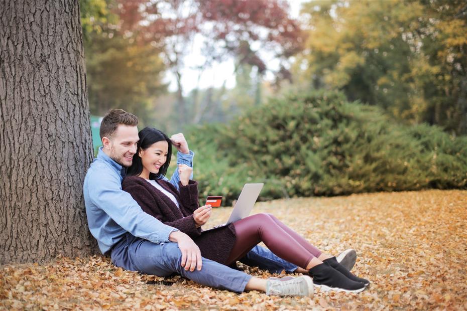 Couple Reclining Beside Tree Trunks using a credit card to buy something online
