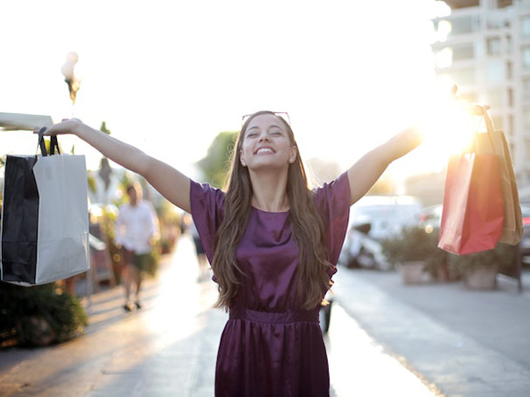 Female outside in purple dress holding her shopping bags up and smiling Female outside in purple dress holding her shopping bags up and smiling