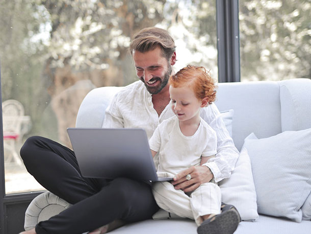 Happy father sitting with child on couch using laptop