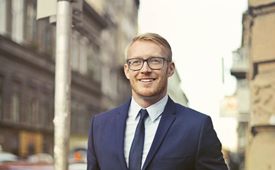 Happy man in black suit and wearing glasses walking through a city