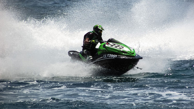 Man wearing a green helmet driving a green jet-ski through a lake spraying water