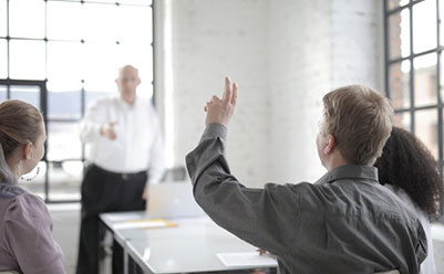 Male employee raising hand for asking question at conference in office boardroom