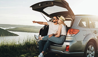 Happy young couple sitting on the tailgate of their SUV  at a scenic overlook