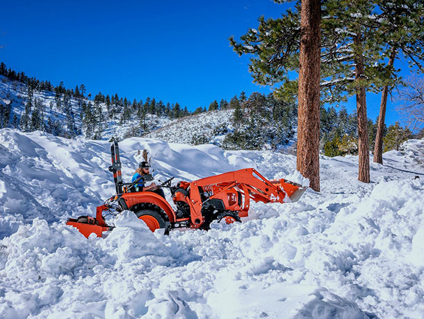 Person in orange shovel vehicle shoveling snow