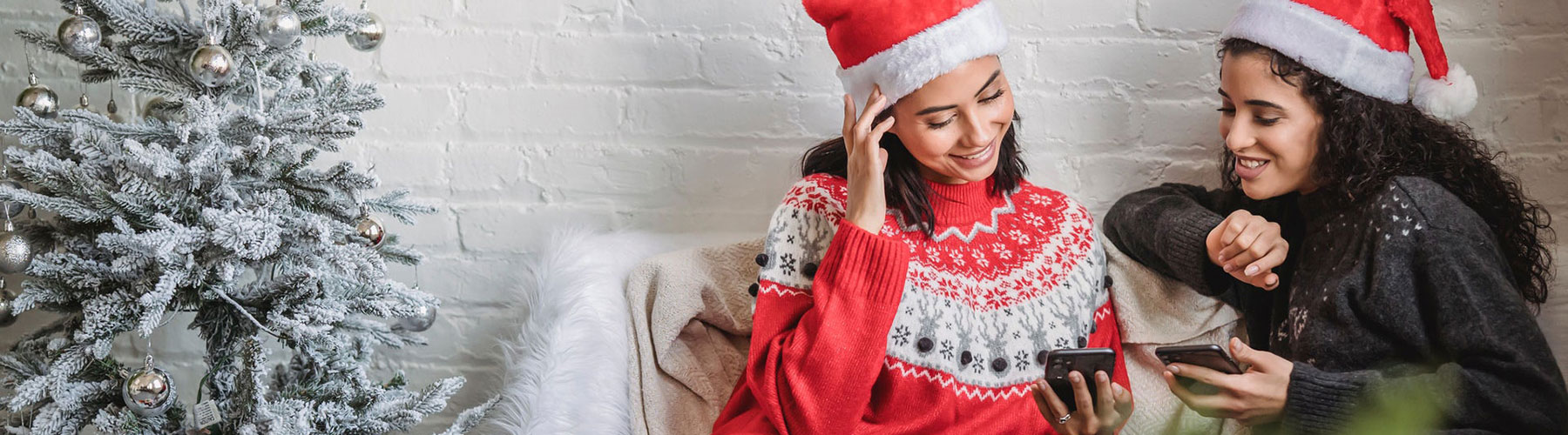 Cheerful women in Santa hats using smartphones together